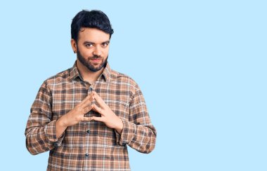 Latin asıllı genç adam rahat ve neşeli gülümseyerek ellerini birleştirip gülümsedi. Başarı ve iyimserlik 