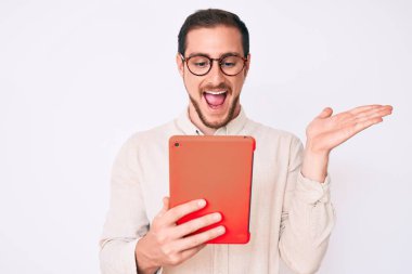 Genç yakışıklı adam zaferi kutlamak için dokunmatik bir cihaz kullanıyor mutlu bir gülümseme ve kaldırılmış ellerle kazanan bir ifadeyle. 