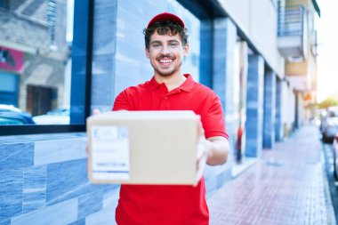 Beyaz tenli genç teslimatçı elinde karton paketle şehre doğru yürüdüğü için mutlu..