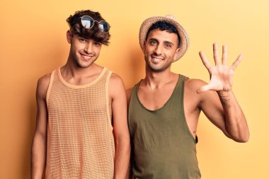 Genç eşcinsel çift yaz kıyafetleri giyip beş numarayı gösteriyorlar ve gülümsüyorlar. Kendinden emin ve mutlular.. 