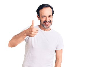 Orta yaşlı yakışıklı bir adam sıradan tişörtler giyip mutlu mesut el hareketi yapıyor. Kameraya bakıp başarıyı gösteren ifade. 