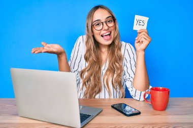 Genç, güzel, sarışın bir kadın elinde evet hatırlatıcısıyla masaya oturmuş başarıyı mutlu bir gülümsemeyle ve kazanan bir ifadeyle el kaldırarak kutluyor. 