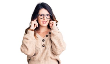 Güzel, genç, esmer bir kadın, gündelik kıyafetler giyip kulaklarını parmaklarıyla kapatıyor ve yüksek sesli müzik sesi için rahatsız edici ifadeler takınıyor. sağır kavramı. 