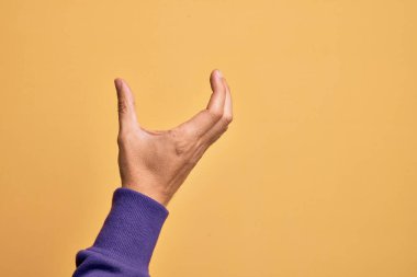 İzole edilmiş sarı arka plan üzerinde parmaklarını gösteren beyaz bir adamın eli. Görünmez bir şeyi alıp, parmaklarıyla uzayı gösteren bir nesneyi tutuyor.