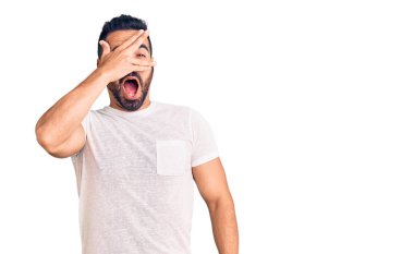 Gündelik kıyafetler giyen genç İspanyol adam şok içinde yüzünü ve gözlerini kapayarak utanmış ifadesiyle parmaklarından bakıyor.. 