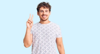 Kıvırcık saçlı, sıradan kıyafetler giyen, kameraya gülümseyen ve zafer işareti yapan genç yakışıklı bir adam. İki numara.. 