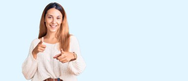 Gündelik giysiler giymiş güzel genç bir kadın mutlu ve komik yüzüyle kamerayı işaret ediyor. iyi enerji ve titreşimler. 