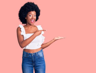 Genç Afrikalı Amerikalı kadın gündelik giysiler giyip kameraya hayret ediyor ve gülümsüyor.. 