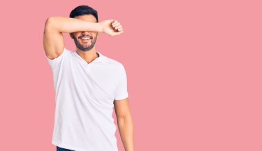 Genç, yakışıklı, günlük kıyafetler giyen, kollarıyla gözlerini kapayan neşeli ve komik gülümseyen bir İspanyol. kör kavram. 