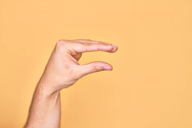 İzole edilmiş sarı arka plan üzerinde parmaklarını gösteren beyaz bir adamın eli. Görünmez bir şeyi alıp, parmaklarıyla uzayı gösteren bir nesneyi tutuyor.
