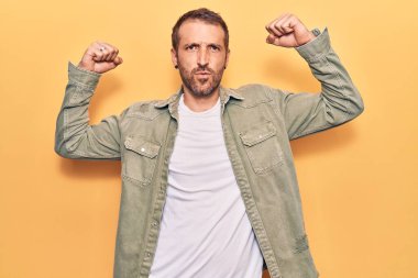 Sıradan kıyafetler giyen genç yakışıklı adam gururla gülümseyen kol kaslarını gösteriyor. fitness konsepti. 