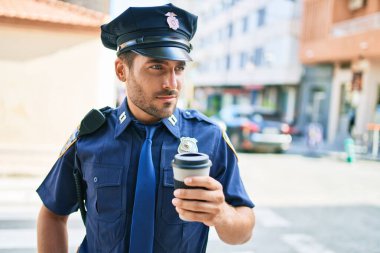 Genç İspanyol polisi ciddi bir ifadeyle polis üniforması giyiyor. Kasaba caddesinde dikilmiş kahve içerken.