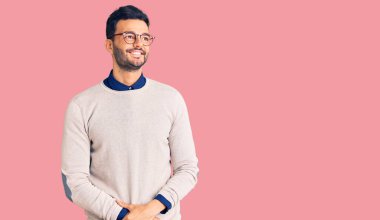 Zarif kıyafetler ve gözlük takan yakışıklı İspanyol bir adam yüzünde gülümseme, doğal bir ifade ile yan yana bakıyor. Kendinden emin gülen. 