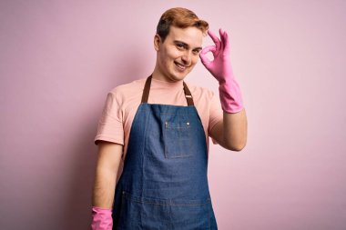 Genç, kızıl saçlı temizlikçi, önlük ve eldivenlerle ev işi yapıyor. Gülümsüyor. El ve parmaklarıyla tamam işareti yapıyor. Başarılı ifade.