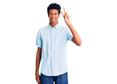 Gündelik giysiler giymiş, gülümseyen, parmaklarını zafer işareti yaparken gösteren genç bir Afro-Amerikan. İki numara.. 