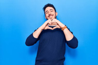 Gündelik giysiler giymiş genç İspanyol bir adam. Sevgiyle gülümsüyor. Elleriyle kalp sembolü ve şekli gösteriyor. romantik kavram. 