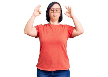 Down sendromlu esmer kadın günlük kıyafetler ve gözlük takıyor rahatlıyor ve gözleri kapalı gülümsüyor parmaklarıyla meditasyon hareketi yapıyor. yoga konsepti. 