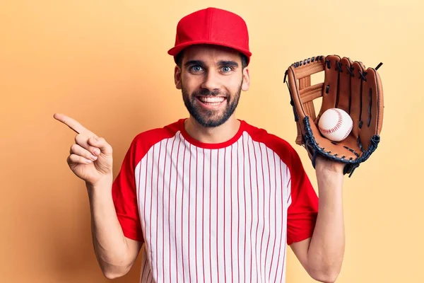 年轻英俊的男子 留着胡子 拿着球和手套打棒球 面带微笑 高兴地手指手画脚地指向一边 — 图库照片