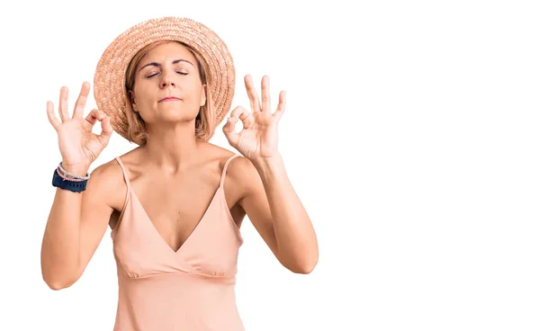 夏の帽子をかぶった若いブロンドの女性がリラックスして笑顔で目を閉じて指で瞑想ジェスチャーをしています ヨガのコンセプト — ストック写真