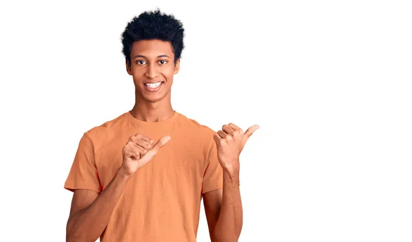 手と親指を上げて後ろを指差すカジュアルな服を着て自信を持って笑っている若いアフリカ系アメリカ人の男 — ストック写真