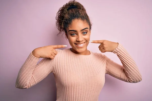ピンクを背景にしたカジュアルなセーターを着た若い美しいアフリカ系アメリカ人の女の子は 明るい表情と指の歯と口で指して笑っています 歯科衛生の概念 — ストック写真