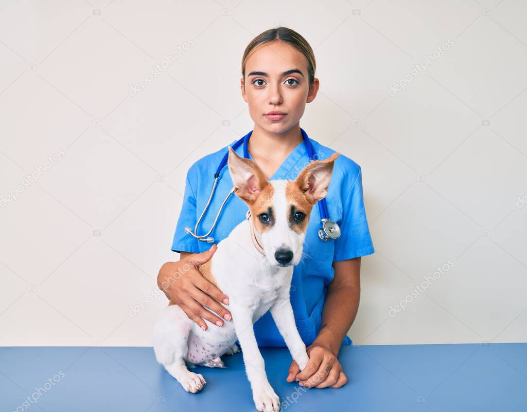 Young beautiful blonde veterinarian woman checking dog health thinking attitude and sober expression looking self confident 