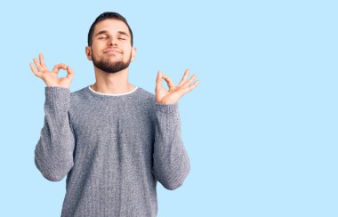 Gündelik kazak giyen genç yakışıklı adam rahatla ve gözleri kapalı gülümse parmaklarıyla meditasyon hareketi yapıyor. yoga konsepti. 