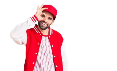 Sakallı, beysbol ceketli ve şapkalı yakışıklı adam gülümsüyor. 