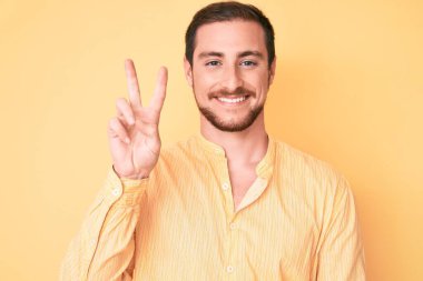 Gündelik kıyafetler giyen genç yakışıklı adam iki numarayı gösterip işaret ederken kendinden emin ve mutlu bir şekilde gülümsüyor.. 