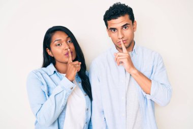 Gündelik kıyafetler giyen genç ve güzel bir Latin çift parmakları dudaklarında sessiz olmak istiyorlar. sessizlik ve gizli konsept. 