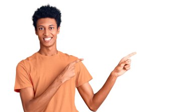 Genç Afro-Amerikalı sıradan kıyafetler giyen, gülümseyen ve kameraya bakan iki elini ve parmağını yana doğru gösteren bir adam.. 