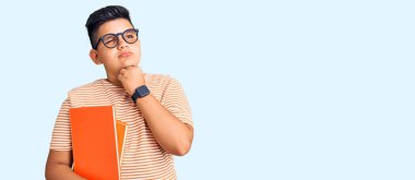 Elleri çenesinde gözlük takan, soru soran, düşünceli bir çocuk. Düşünceli bir yüzle gülümsüyor. şüphe kavramı. 