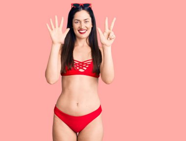 Bikini giyen güzel beyaz bir kadın sekiz numaralı parmaklarıyla gülümseyerek mutlu ve kendinden emin bir şekilde onu işaret ediyor.. 