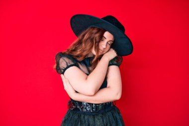 Cadılar bayramı kostümü giyen genç ve güzel bir kadın mutlu ve olumlu bir şekilde kendine sarılıyor, kendinden emin gülümsüyor. Sevgi ve özgüven. 