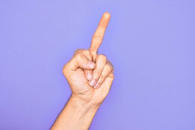 Hand of caucasian young man showing fingers over isolated purple background showing provocative and rude gesture doing fuck you symbol with middle finger