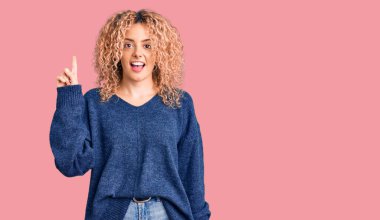 Kış süveteri giyen kıvırcık saçlı genç sarışın kadın başarılı bir fikri işaret ediyor. Heyecanlı ve mutlu. Bir numara.. 