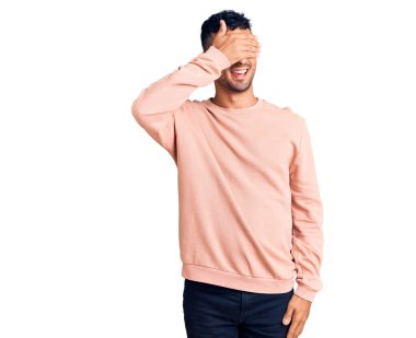 Gündelik kıyafetler giyen, gülümseyen ve gülümseyen genç İspanyol adam şaşırmak için gözlerini kapatıyor. kör kavram. 