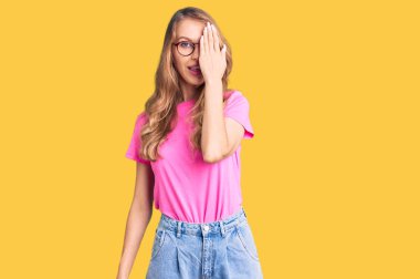 Sarışın, güzel, beyaz bir kadın. Günlük kıyafetler ve gözlük takıyor. Bir gözünü eliyle kapatıyor.. 