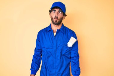 Kıvırcık saçlı, ayı kılıklı, işçi tulumu giyen, dudağıyla balık suratı yapan yakışıklı bir genç adam. Komik ifade. 