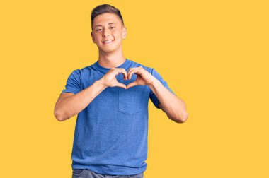 Gündelik giysiler giyen genç, yakışıklı İspanyol bir adam. Sevgiyle gülümsüyor. Kalp sembolü ve elleri ile şekil veriyor. romantik kavram. 