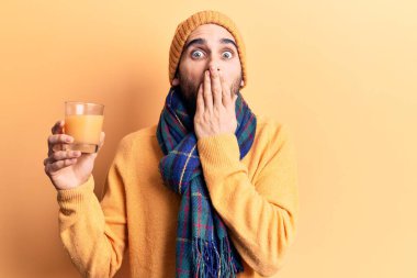 Sakallı, atkı takan, yün şapkalı, portakal suyu içen, ağzı ağızla kaplı, şok olmuş ve hata yapmaktan korkan genç yakışıklı bir adam. şaşırmış ifade 