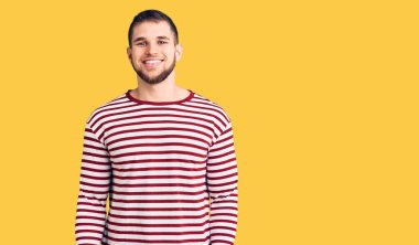 Genç yakışıklı adam çizgili kazak giyiyor ve yüzünde mutlu ve havalı bir gülümseme var. şanslı kişi. 