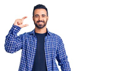 Gündelik kıyafetler giyen, gülümseyen, kendine güvenen, el hareketi yapan, parmaklarıyla işaret yapan ve kameraya bakan genç İspanyol bir adam. ölçüm kavramı. 