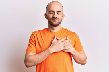 Genç, kel, sıradan tişörtler giyen, elleri göğsünde, gözleri kapalı, yüzünde minnet dolu bir jest ile gülümseyen bir adam. sağlık kavramı. 