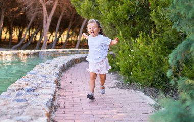 Sevimli sarışın çocuk mutlu gülümsüyor. Yüzünde gülümsemeyle parkta koşuşturuyor.