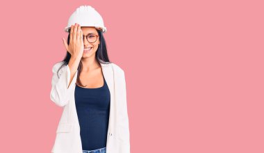 Mimar şapkası takan genç ve güzel bir Latin kız ve gözlük takıyor. Bir gözünü eliyle kapatıyor. Yüzünde kendine güvenen bir gülümseme ve şaşırtıcı bir duygu var.. 