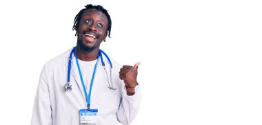 Doktor steteskop ve kimlik kartı takan, gülümseyen ve baş parmağıyla yüzünü gösteren genç, Afro-Amerikan bir adam.. 