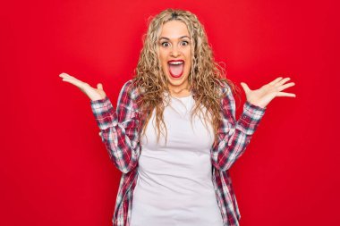 Genç ve güzel sarışın bir kadın yalnız kırmızı arka planda dikilmiş çılgın ve başarıyı kollarını kaldırarak ve heyecanla haykırarak kutluyor. Kazanan konsept