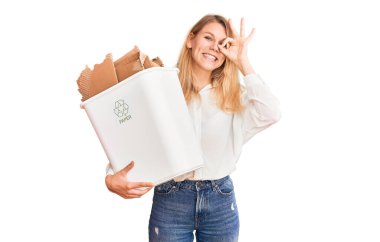 Geri dönüşüm kâğıdı kutusunu tutan güzel sarışın kadın gülümsüyor. 