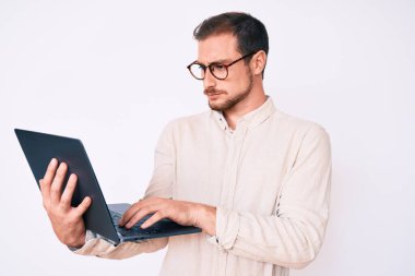 Genç yakışıklı adam dizüstü bilgisayar tutuyor. Düşünme tarzı ve ayık yüz ifadesi. Kendine güveni tam görünüyor. 